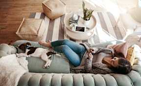 A woman is lying on a couch with her dog at The Woodlands Apartments, Milton Keynes