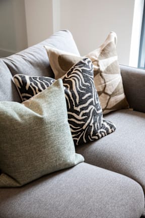 A grey couch with four pillows on it.
