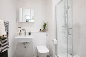 A white bathroom with a toilet, sink, mirror, and shower.