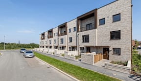 A row of modern apartment buildings with cars parked on the street at Origins Apartments, Cambridge, CB3 0UX