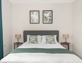 A bed with a white comforter and two green throw pillows at Origins Apartments, Cambridge