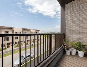 A balcony with a black railing and potted plants overlooks a street with cars and houses at Origins Apartments, Cambridge, CB3 0UX
