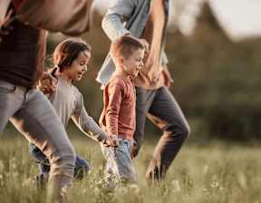 A group of people, including children, are playing in a grassy field at Origins Apartments, Cambridge, CB3 0UX