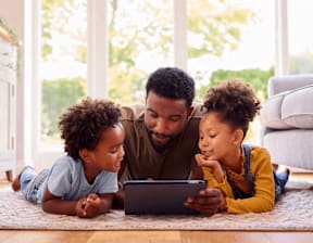 A man and two children are lying on the floor looking at a tablet at Origins Apartments, Cambridge