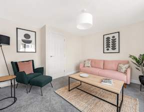 A living room with a pink couch, green chair, and a coffee table at Origins Apartments, Cambridge, CB3 0UX