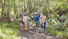 A family of five walking a dog on a trail in the woods at The Woodlands Apartments, Milton Keynes
