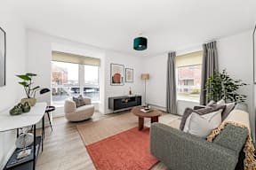 A living room with a grey couch and a red rug at The Woodlands Apartments, Milton Keynes, MK5 6GS