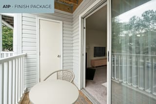 A white table and chair are on a deck with a glass door leading to a living room