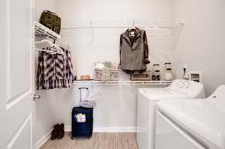 A small bathroom with a white sink, a blue suitcase, and a brown jacket hanging on the wall.