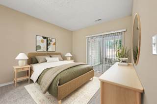 A bedroom with a bed, nightstand, lamp, and a mirror on the wall.