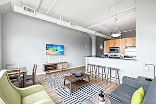 a living room with a couch a table and a chair and a kitchen with a sink and