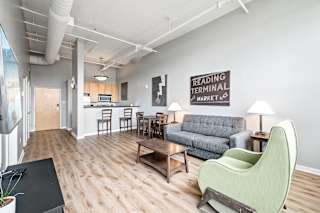 a living room with a couch a chair a table and a kitchen in the background