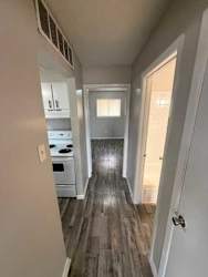 A long hallway with a kitchen area on the left and a doorway leading to another room on the right.