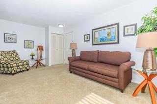 A living room with a brown couch, a chair with a patterned cushion, and a small table with a lamp.