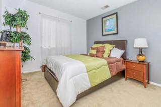 A bedroom with a bed, nightstand, and a potted plant.