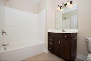 A bathroom with a white tub, brown cabinets, and a white toilet.