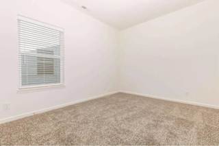A room with a carpeted floor and a window with blinds.