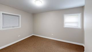 A room with a carpeted floor and two windows.