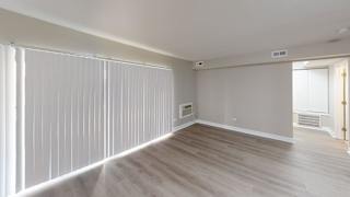 A room with a window covered by white blinds and a wooden floor.