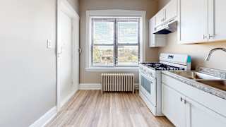 A kitchen with white cabinets and a window with blinds.