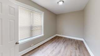 A room with a window covered by blinds and a wooden floor.