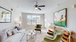 A living room with a grey couch, a green chair, and a painting on the wall at The Slate, Jeffersonville, 47130