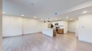 A spacious room with a kitchen area in the background.