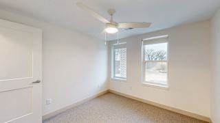 A room with a ceiling fan and two windows.