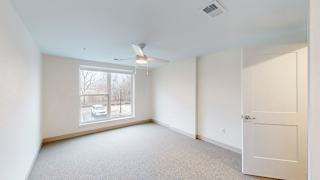 A room with a white door, carpeted floor, and a window showing a view of a car and trees outside.