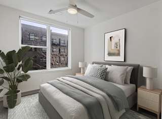A bedroom with a large bed, a ceiling fan, and a window overlooking a cityscape.