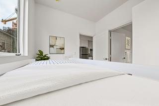 A white bed with a white mattress is in the foreground of a room with white walls.