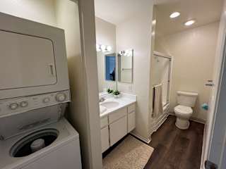 A white washing machine is in a small bathroom with a toilet and sink.