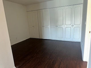 A room with white cupboards and brown flooring.