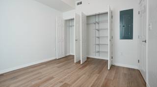 A room with white walls and wooden flooring, featuring a built-in shelving unit and a doorway leading to another room.