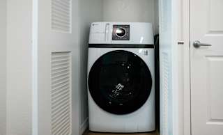 A white washing machine is tucked into a small space between a door and a wall.