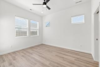 A room with a ceiling fan and two windows.