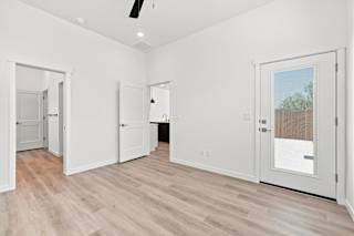 A room with white walls and wooden flooring, with a ceiling fan and a door leading outside.