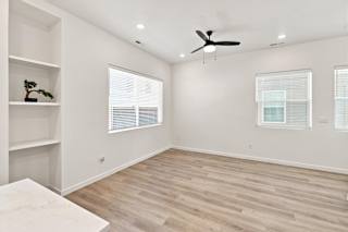 A room with a ceiling fan and two windows with blinds.