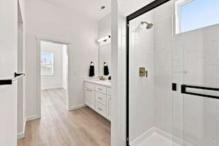 A bathroom with a white tile shower and a white vanity with a mirror.