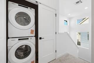 Stacked white washing machine and dryer in laundry room at Alante Homes at Spring Run, Caldwell, 83607