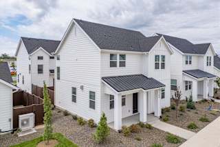 A white house with a black roof is surrounded by other similar houses. at Alante Homes at Spring Run, Caldwell