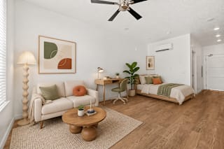 A living room with a white couch, a wooden coffee table, and a bed with a green blanket.