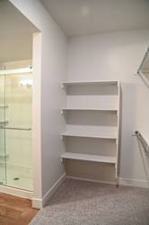 A white shelving unit in a corner of a room with a glass door.
