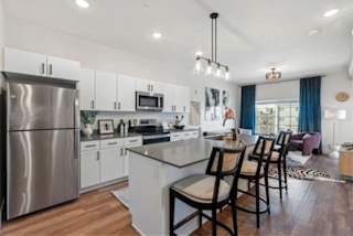 A modern kitchen with a stainless steel refrigerator and a central island with chairs.