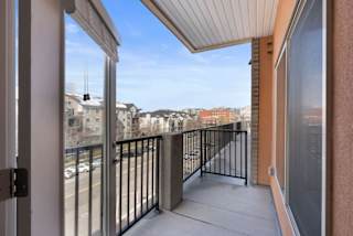 A balcony with a black railing and a view of buildings and cars.