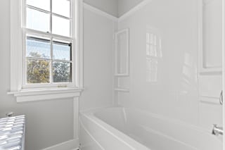 A white bathroom with a window and a bathtub.