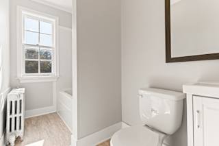 A white toilet sits next to a window in a bathroom.