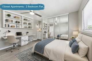 A bedroom digitally staged with a bed, rug, decor, and office chair. Bedroom includes built in desk with drawers, shelving above desk, built in dresser next to mirrored closet doors. Vinyl plank flooring, ceiling fan, and horizontal window across from desk and shelves.