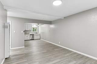 A spacious living room with vinyl plank flooring and a kitchen in the background.