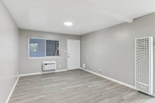 A living room with a window, a door, and a wall-mounted air conditioner unit.
